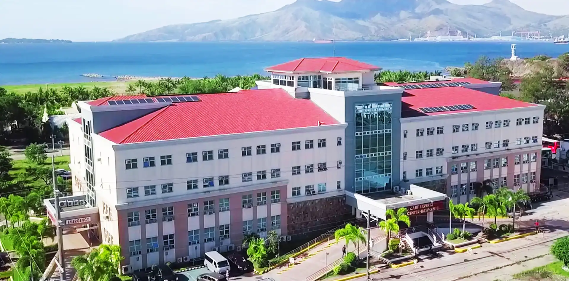 ACE Medical Center Baypointe from the air, its red roofs facing Subic Bay with the mountains beyond.