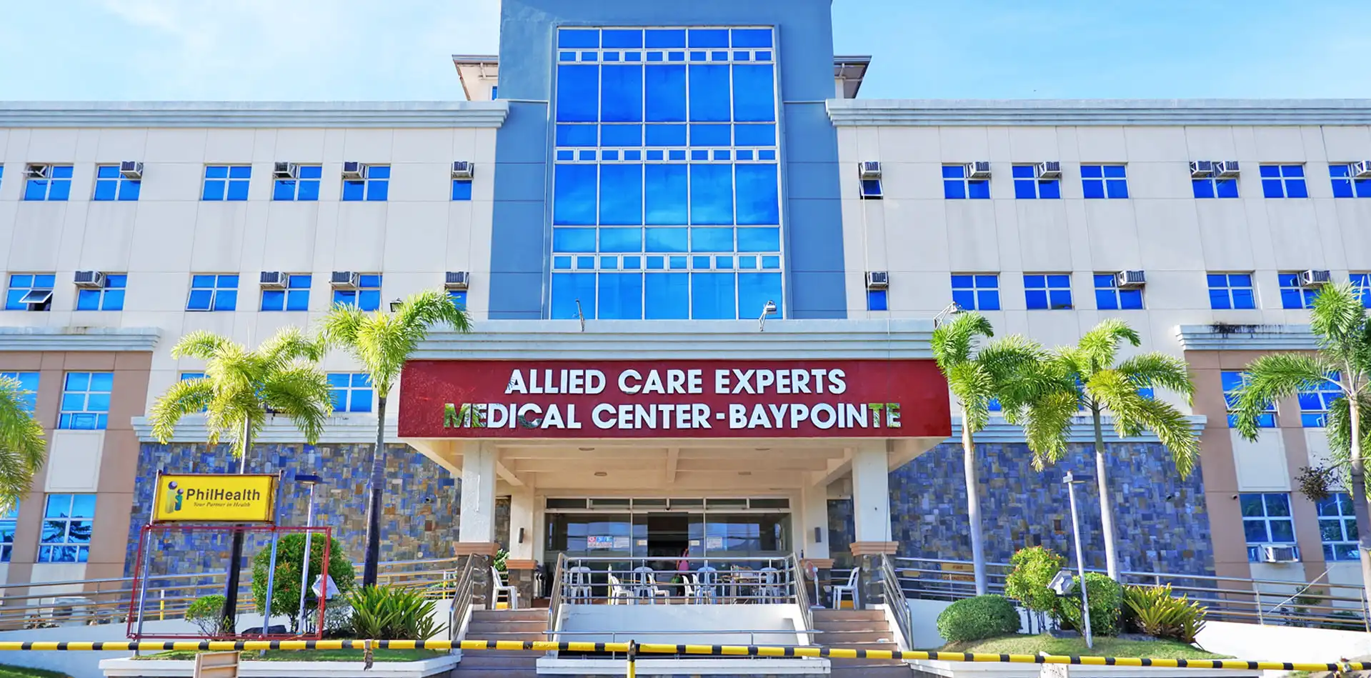 The main entrance beneath the Allied Care Experts Medical Center Baypointe sign, with palms either side of the steps.